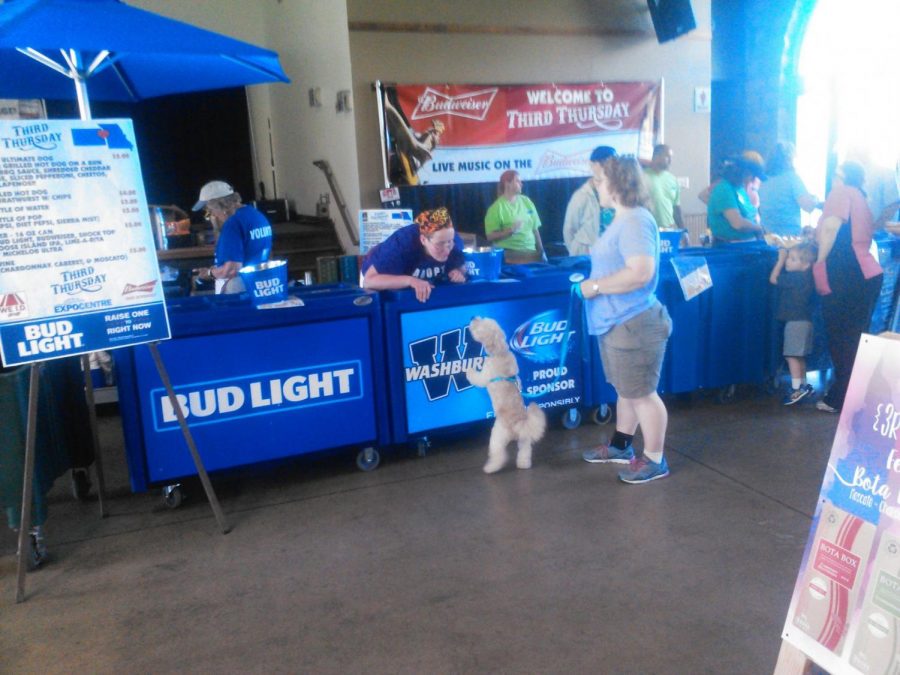 A small dog steps up to greet a woman at a booth at Third Thursday.