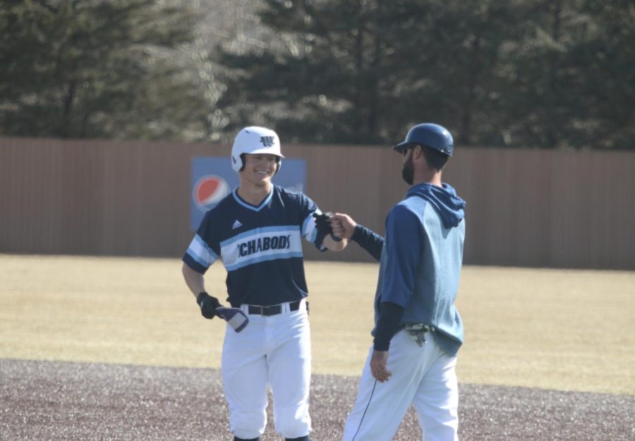 Senior Brett Ingram fist bumps assistant coach Connor Crimmins after reaching first base Feb. 28, 2022. Ingram had four hits in the game.