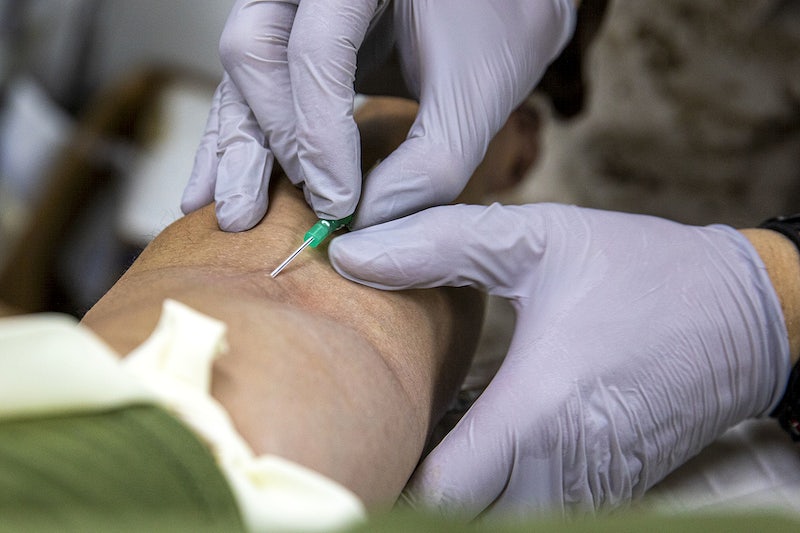 A medical professional inserts a needle into a patients arm to draw blood. Usually about a pint of blood is drawn for donation.