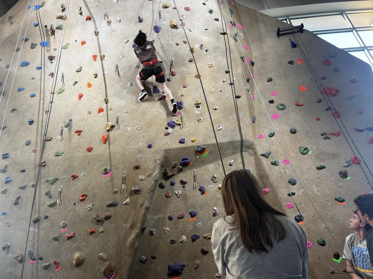 A student employee holds the climber's weight as he goes up the rock wall. The climber made it to the top with the employee’s guidance.