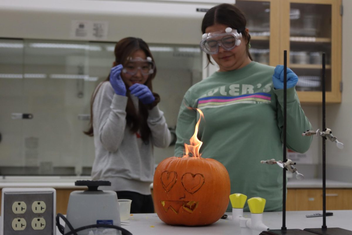 Kayleen Awh and Myrrah Awwad, freshman biology majors, react as a jack-o’-lantern ignites during the experiment. The students used water and calcium carbide to create an explosive chemical reaction.