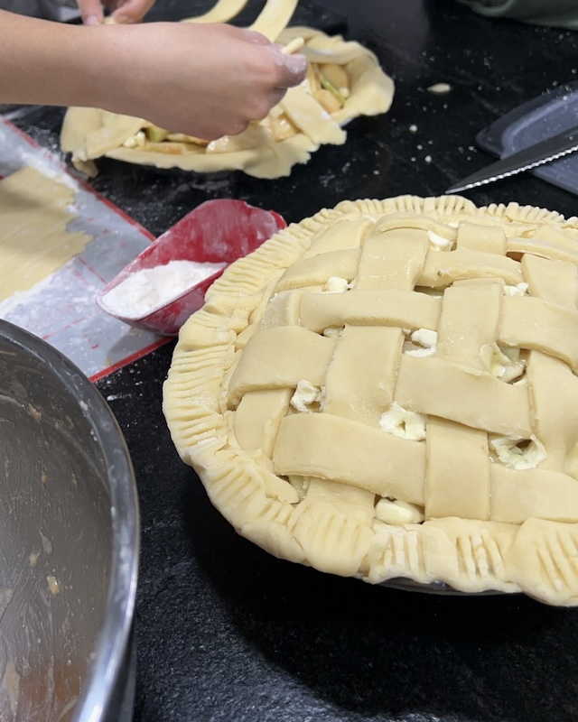 Crafting a lattice crust adds a decorative touch to the apple pie. Earlier, fresh apple slices were prepared and seasoned for the fillings.