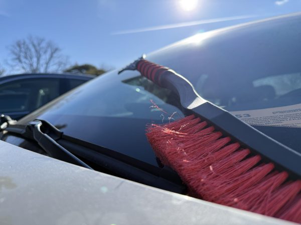 An ice scraper sits on the front windshield of a car. They can be bought in many retail stores and are a useful tool to clear ice off the windows.