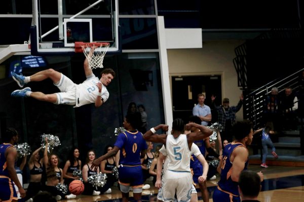 Tyson Rudd, redshirt freshman guard, slam dunks the ball during the game against the University of Nebraska-Kearney defenders. Rudd’s dunk electrified the crowd and set the tone for his team's victory.