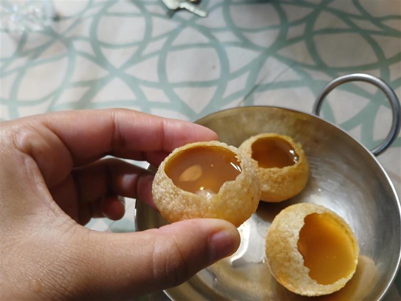 A small hole is made in the fried puri. Gravy and water were added inside the puri, making it ready to eat.
